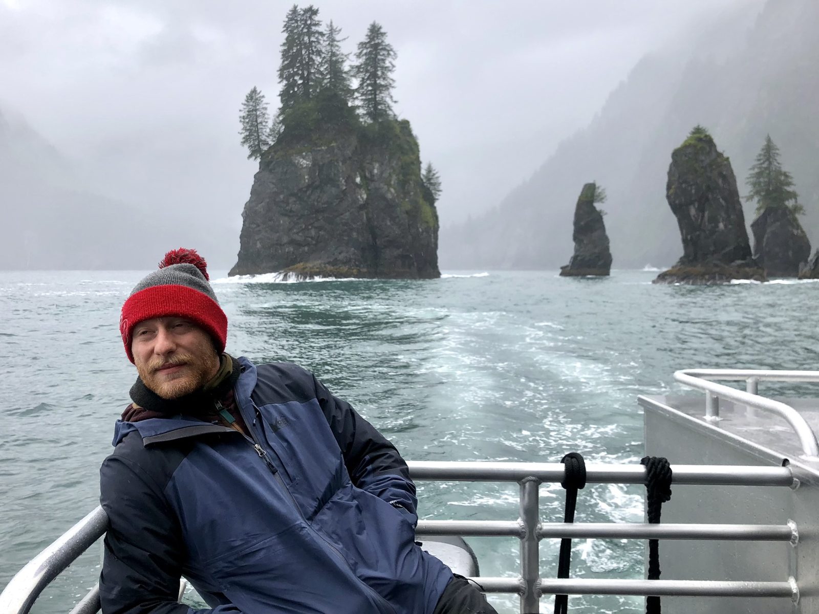 Owen on a boat deck in a misty fjord, with forested sea stacks behind him
